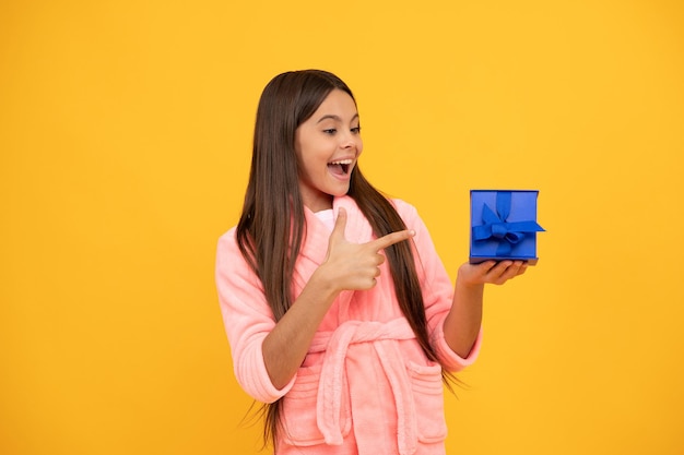 Happy teen girl in home terry bathrobe pointing finger on gift or present box, presenting product.