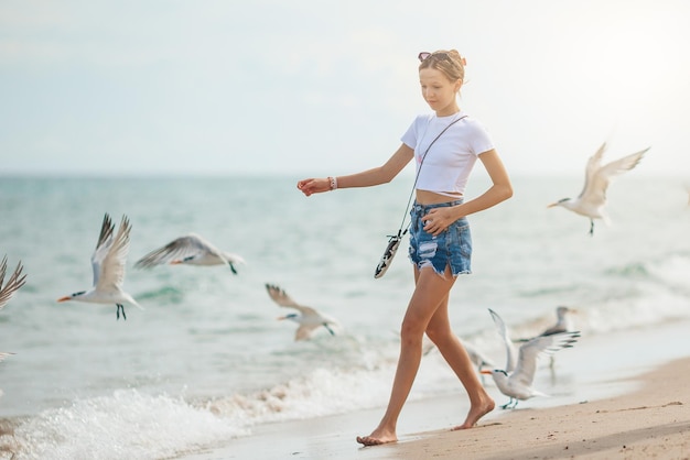 Happy teen girl playing with seagull birds running and having fun on the beach on a hot summer day Florida summer holiday vacation