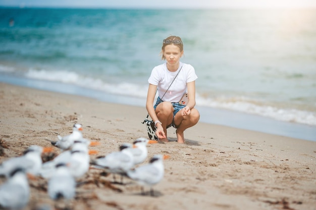 Happy teen girl playing with seagull birds running and having fun on the beach on a hot summer day Florida summer holiday vacation