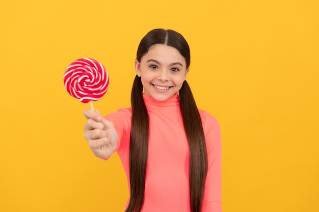 Happy teen girl with lollipop candy on stick on yellow background candy shop