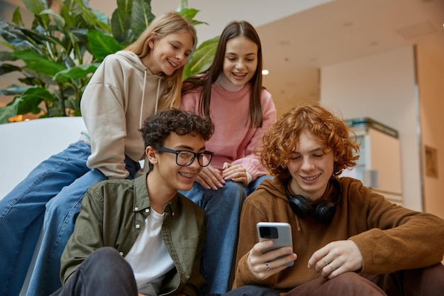 Happy teenage friends watching funny video on smartphone at shopping mall