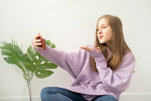 Happy teenage girl holding mobile phone and blowing kiss while having video chat, taking selfie at home.