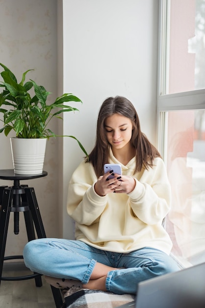 Happy teenage girl looking at smartphone relaxing at home enjoy using mobile online apps playing games on mobile phone checking messages or social media messages Soft selective focus