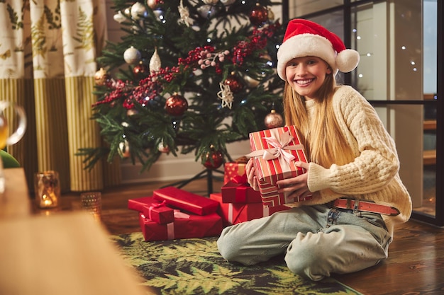 Happy teenage girl sitting at Christmas tree