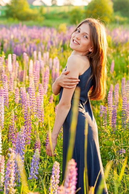 Happy teenage girl smiling outdoor. Beautiful young teen woman resting on summer field with blooming wild flowers green background