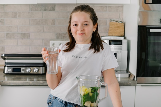 Happy teenager cooking healthy green smoothie with fresh fruits and greens spinach at home