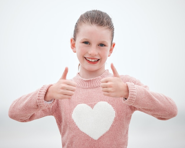 Happy teenager girl and hands in thumbs up with smile for gesture sign or symbol against a grey background Portrait of female teen smiling with hand for okay yes or great emoji in happiness