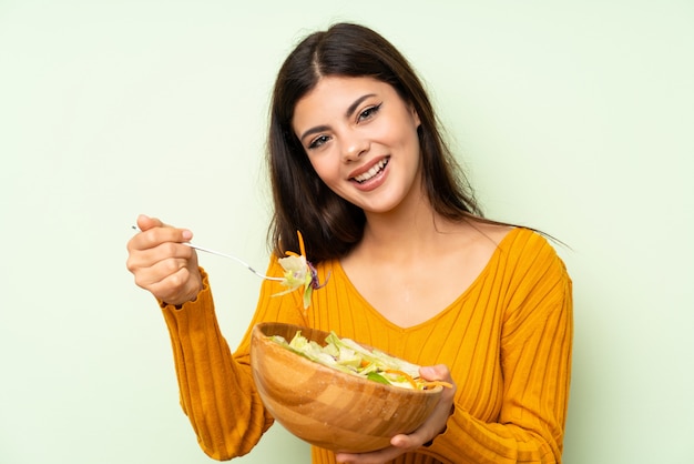 Happy Teenager girl with salad over green wall