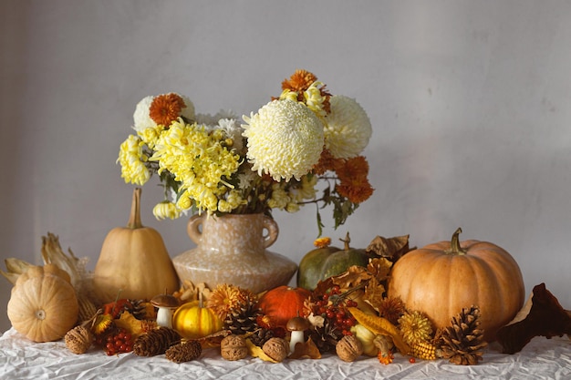 Photo happy thanksgiving autumn still life pumpkins and chrysanthemum in vase fall leaves berries and pine cones on table fall harvest background space for text