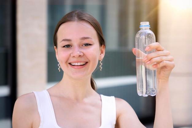 happy thirsty woman is drinking pure fresh water from bottle at warm summer day outdoors smiling