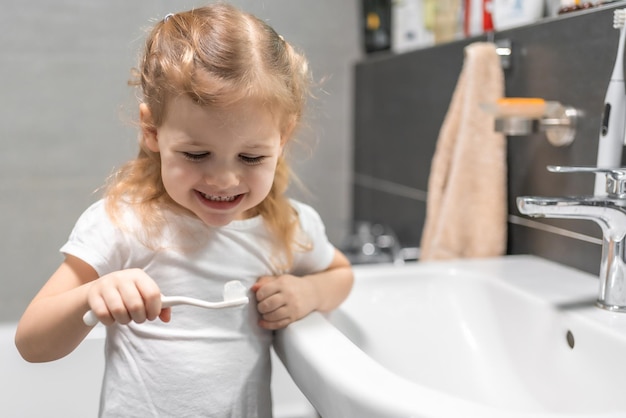 Happy toddler girl brushing teeth in the bath