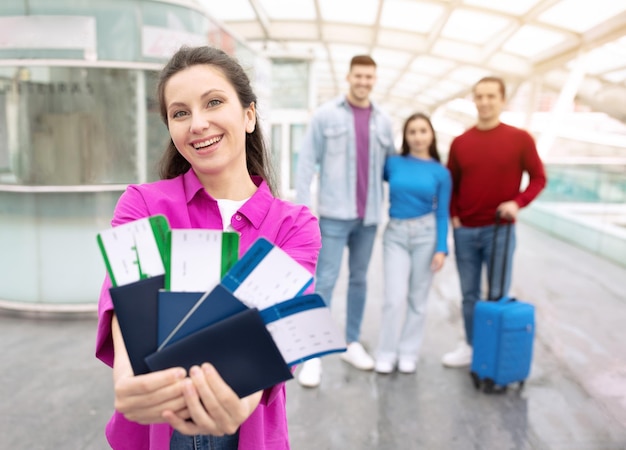 Happy tourist woman showing tickets traveling with friends in airport