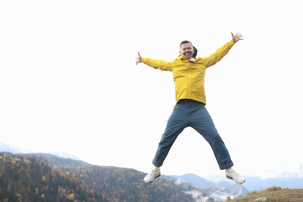 Happy tourist in yellow coat smiling and jumping with open arms mountains and forest in