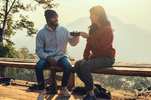 Happy traveler couple resting on mountains in sunrise with drinking coffee