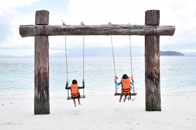 Happy traveler Kid in Life jacket relaxing on swing and looking beautiful nature seascape