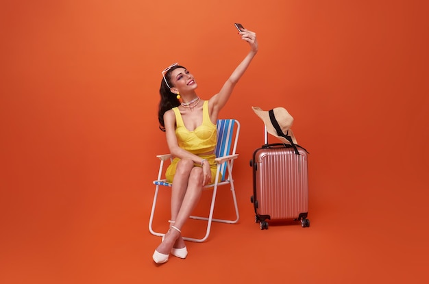 Happy traveler tourist woman sitting on chair with suitcase do selfie on mobile cell phone