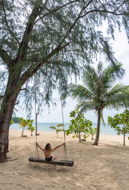 Happy traveler woman in hammock relaxing on the swing and looking beautiful nature and beach