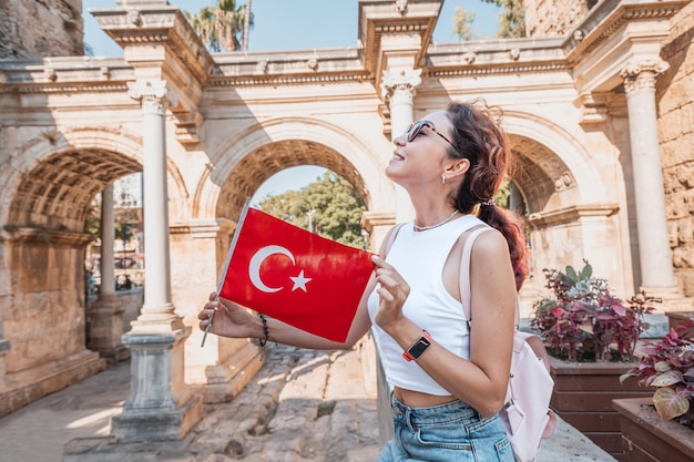 Happy traveller girl with turkish flag in hand and famous gate or Hadrian arch in Antalya National holiday and mustvisit tourist and sightseeing sites in Turkey