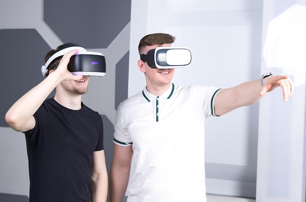 Happy two 2 men positive smiling guys using wearing virtual reality headset mask or 3D AR VR glasses