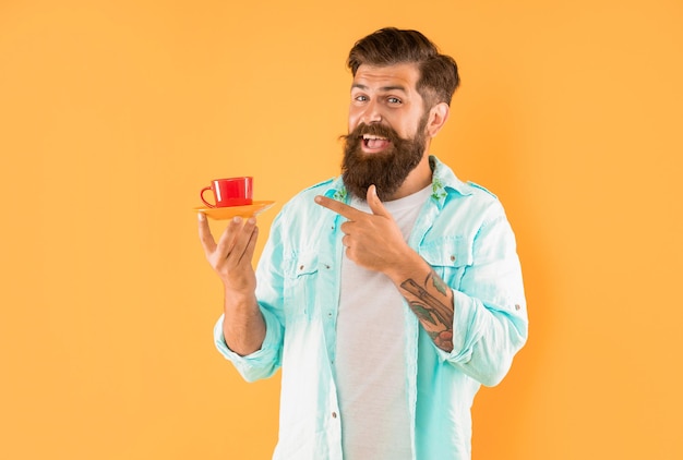 Happy unshaven man in shirt point finger on coffee on yellow background coffee cup