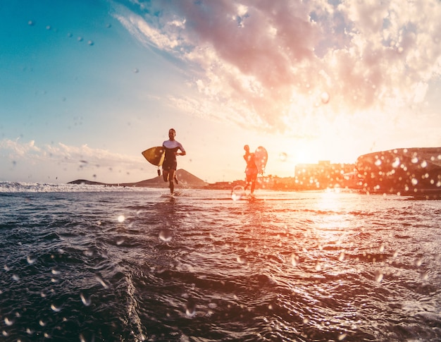 Happy urfers running with surf boards on the beach