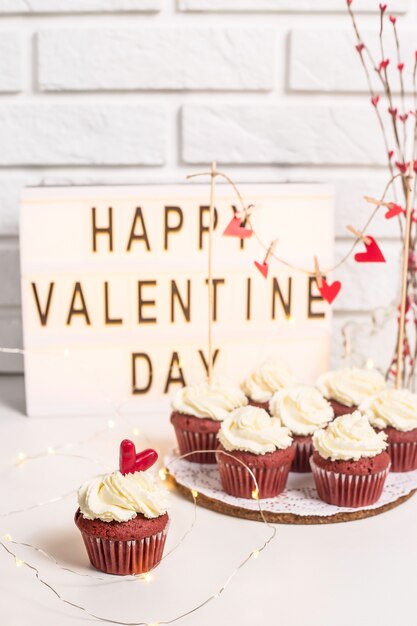 Happy Valentine's Day is written on a decorative lamp next to red cupcakes