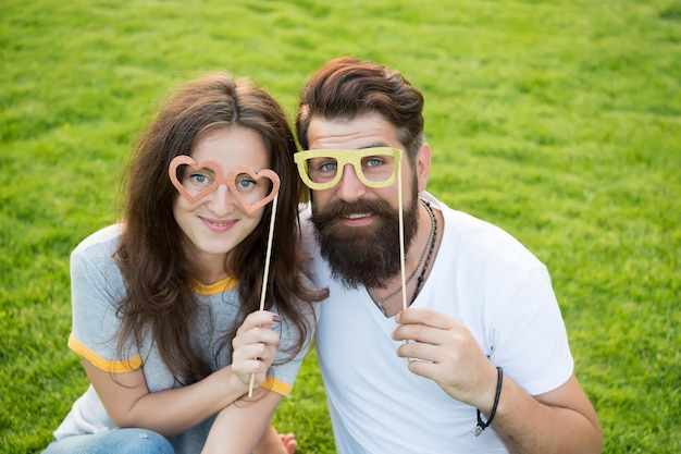 Happy valentines day. Couple in love happy smiling with party glasses on green grass. Happy family holding photobooth props on stick. Enjoying happy celebration.