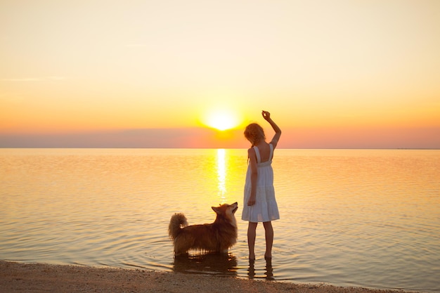 Happy weekend by the sea - little girl is walking with a dog by the sea at sunset. Ukrainian landscape at the Sea of Azov, Ukraine