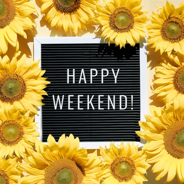 Happy Weekend, text on letter board with sunflowers. Flat lay with natural flowers and motivation words on black letterboard. Top view from above, square composition.