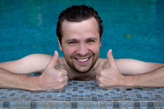 Happy wet caucasian man in swimming pool shows thumbs up