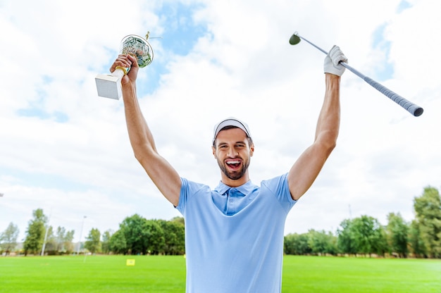 Photo happy winner. happy male golfer holding trophy and driver while standing on golf course