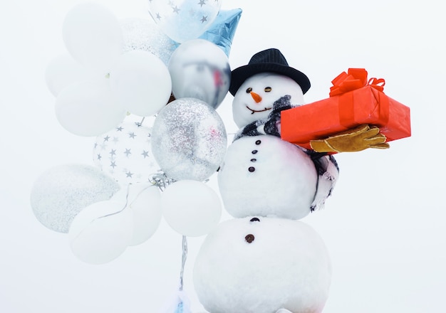 Photo happy winter time. snowman with balloons and gift. snow man in hat, scarf, gloves.