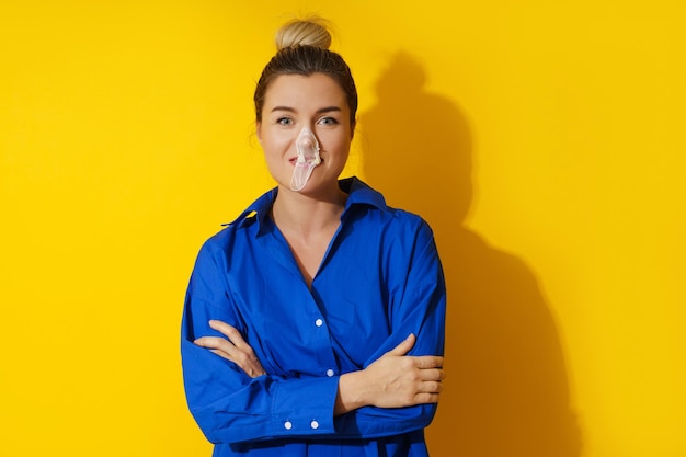 Happy woman blowing a bubble with chewing gum against yellow background