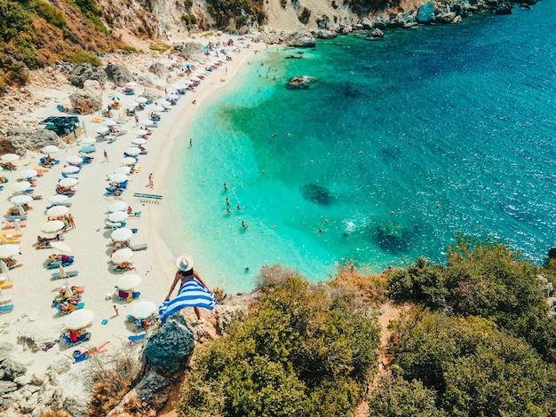 Happy woman in blue swimsuit holding greece flag at the top of the cliff