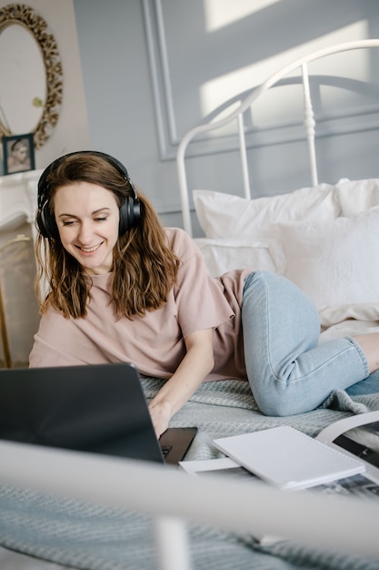 Happy woman in casual with the headphones working on a laptop remotely from home