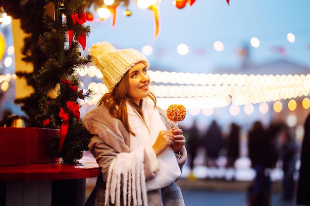 Happy woman on Christmas market with caramelized apple. Outdoor activities on Christmas.