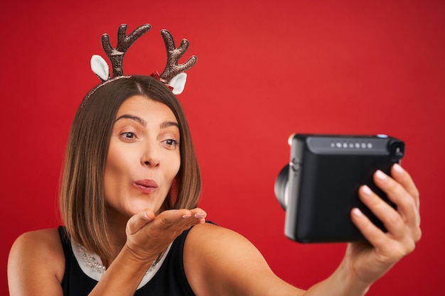 happy woman in Christmas mood taking instant pictures over red background