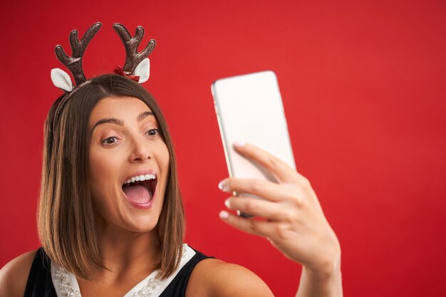 happy woman in Christmas mood taking selfie over red background