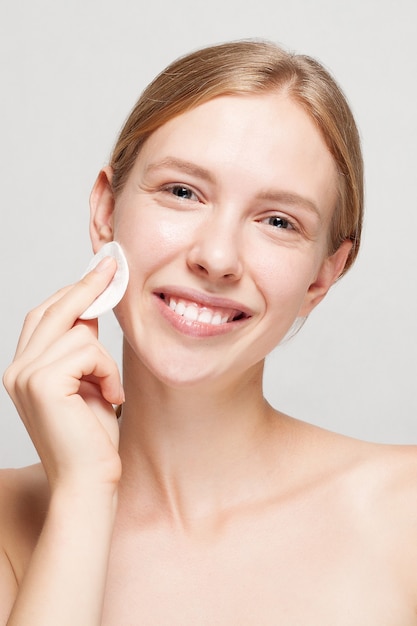 Happy woman cleaning her face with cotton pads