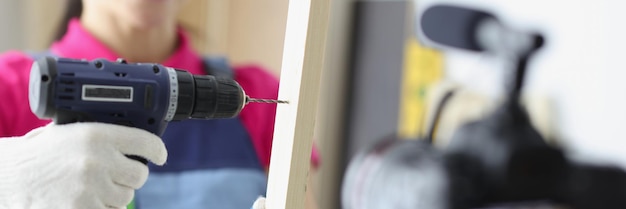 Happy woman construction site worker use drill to make hole in wooden plank