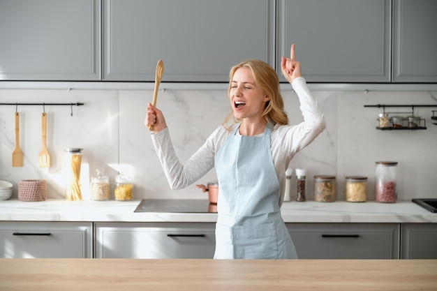 Photo happy woman dancing on kitchen singing having fun at home