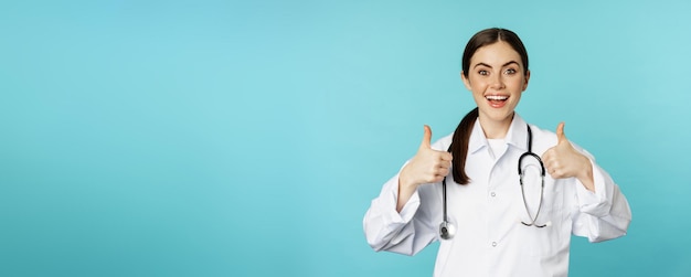 Photo happy woman doctor medical worker in white coat showing thumbs up in approval like something praise