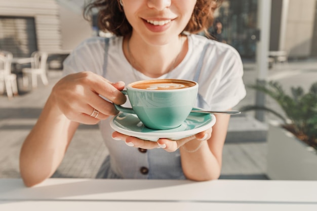 A happy woman drinks a fragrant fresh cappuccino coffee in an outdoor cafe on the terrace The concept of leisure and a break for rest