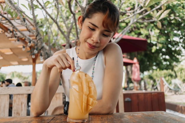 Happy woman drinks mango juice smoothie in summer day