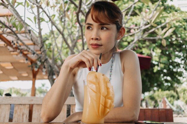 Happy woman drinks mango juice smoothie in summer day