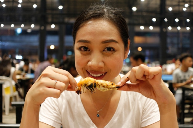 Happy woman eat grilled shrimp with a delicious bite face.