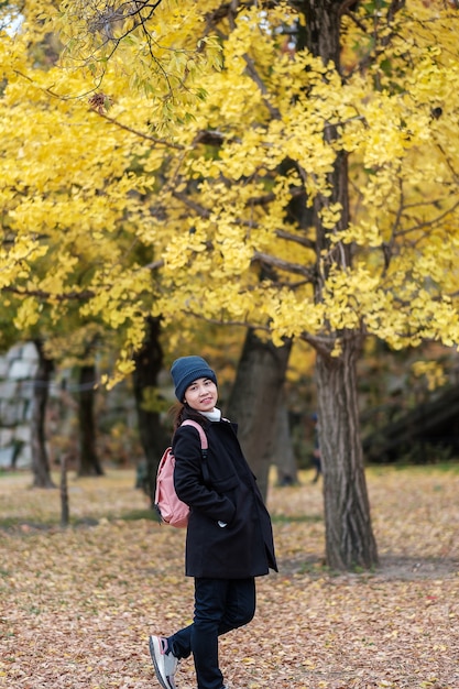 Happy woman enjoy at the park outdoor in Autumn season, Asian traveler in coat and hat against Yellow Ginkgo Leaves background