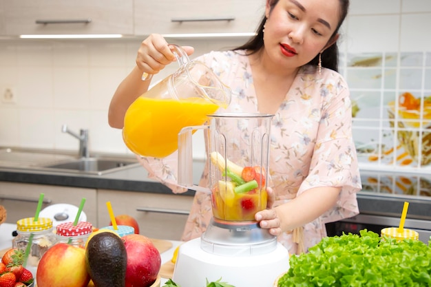 Happy woman enjoy preparing freshly squeezed fruits with vegetables for making smoothies for breakfast together in the kitchen.diet and Health concept.