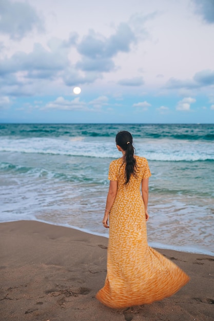 Happy woman enjoying beautiful sunset with big full moon on the beach