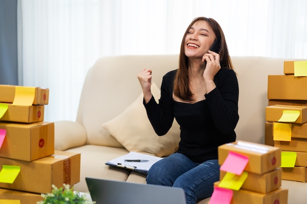 Happy woman entrepreneur talking on a smartphone and using laptop computer to selling product online at home office